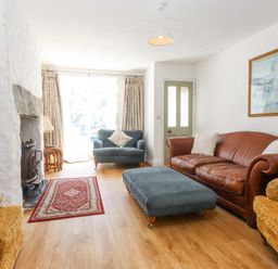 A living room with a leather sofa blue armchair and ottoman a fireplace and framed art at Llys Emrys in Beddgelert