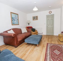 A living room with a brown leather sofa blue ottoman armchair and a red patterned rug at Llys Emrys in Beddgelert