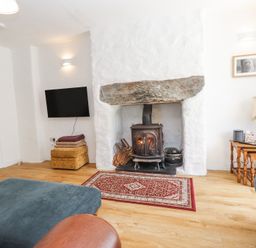 A living room with a wood burning stove rug television and seating at Llys Emrys in Beddgelert