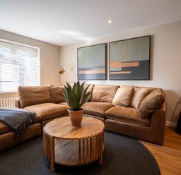 A living room with a brown sectional sofa wooden round coffee table and two abstract paintings at The Reef in Kessingland