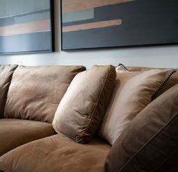 A brown sofa with cushions and abstract paintings on the wall at The Reef in Kessingland
