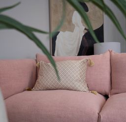 A pink sofa with a patterned cushion a lamp and a painting in the background at Coral Cottage in Kessingland