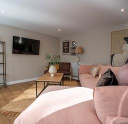 A living room with a pink sofa a wooden coffee table and a wall-mounted tv at Coral Cottage in Kessingland