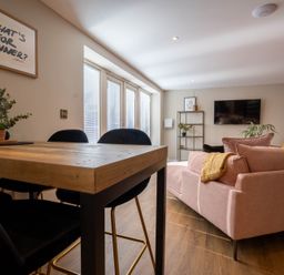A dining table with black chairs and a pink sofa in a living room at Coral Cottage in Kessingland