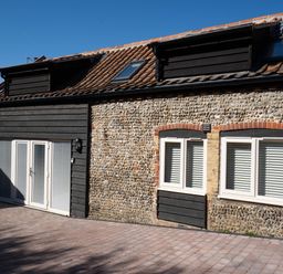 Exterior of a building with cobblestone and dark wood panel walls with windows and double glass doors at Coral Cottage in Kessingland