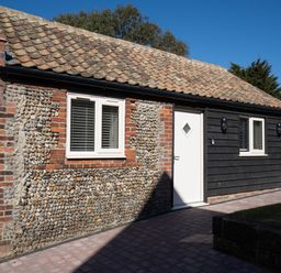 A building exterior with tiled roof white doors and windows and pebble and brick walls at Dunes Cottage in Kessingland