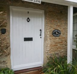 A white door with the number 3 and a black door knocker on a stone cottage wall with a sign reading Cobblers Cottage Langton Herring
