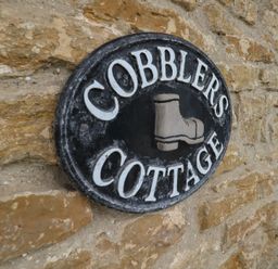 A round black sign with white letters reading Cobblers Cottage and a boot image on a stone wall at Cobblers Cottage in Langton Herring