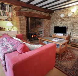 A living room with a red sofa a fireplace a wooden coffee table and a television at Cobblers Cottage in Langton Herring