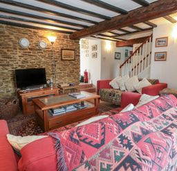A living room with red sofas a wooden coffee table a TV on a wooden stand and a staircase at Cobblers Cottage in Langton Herring