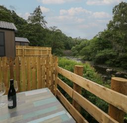 An outdoor seating area with a table, glasses, and a bottle at Woof Luxury Family Pod in Keswick