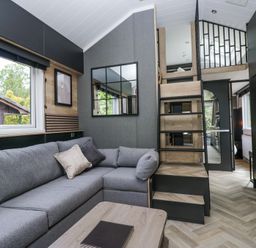 A living room with a gray sofa and a wooden coffee table next to stairs leading to a loft at Lingy Luxury Family Pod in Keswick