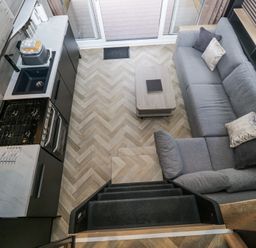 A small kitchen and living area with a grey sofa, coffee table, and stove viewed from above at Lingy Luxury Family Pod in Keswick