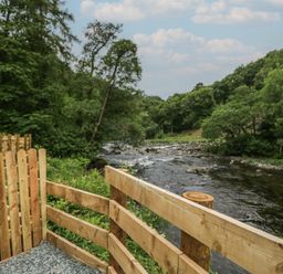 A river surrounded by trees and a wooden fence at Lingy Luxury Family Pod in Keswick