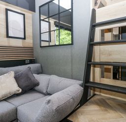 A corner of a room with a gray sofa cushions wall art and a black ladder at Sail Luxury Family Pod in Keswick