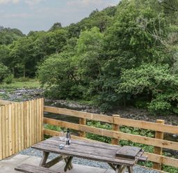 An outdoor seating area with a table and chairs near a river at Sail Luxury Family Pod in Keswick