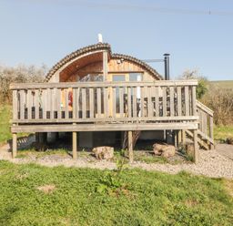 A wooden pod cabin with a deck and outdoor chairs on grass and gravel at Cabanau Bach in Bedwas