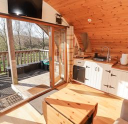 A small kitchen with wooden cabinets and countertop next to glass doors leading to a wooden deck at Cabanau Bach in Bedwas