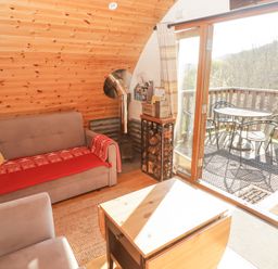 A small living room with a sofa a chair a coffee table a wood stove and a door leading to a balcony with a table and chairs at Cabanau Bach in Bedwas