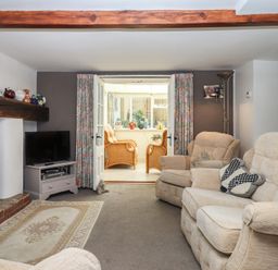 A living room with beige armchairs a television floral curtains and a small sitting area beyond at Badger's Den in Budleigh Salterton