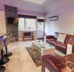 A living room with leather sofas a glass coffee table bar stools and a wall mounted television at 1 The Old Coach House in Ambleside