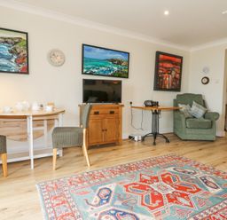 A living room with patterned rug chairs small tables armchair and paintings on walls at Carningli Suite near Newport