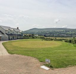 A golf tee area with a sign indicating 10th tee and houses beside it near a grassy landscape and hills in the background at Carningli Suite near Newport