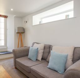A living room with a grey sofa and cushions next to a window and a floor lamp at St Georges in Padstow
