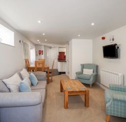 A living room with a grey sofa and blue armchairs with pillows a wooden coffee table and dining table with chairs at St Georges in Padstow