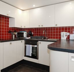 A kitchen with white cabinets red tiled backsplash and black countertops at St Georges in Padstow