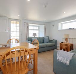 A room with two blue sofas a wooden dining table with four chairs a side table with lamp and windows at St Saviours in Padstow