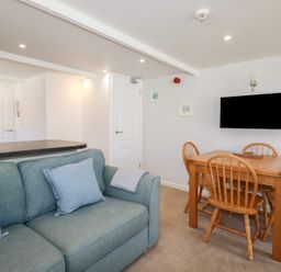 A living room with a blue sofa and wooden dining table with four chairs and a wall-mounted TV at St Saviours Padstow