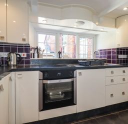 A kitchen with white cabinets black countertops a built in oven a kettle a toaster and a microwave at St Saviours in Padstow