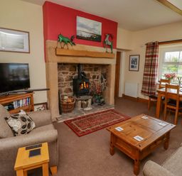 A living room with a stone fireplace wooden furniture and a window with plaid curtains at Folly View in Eglingham