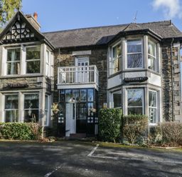 A stone building with large bay windows and a small balcony at Fir Trees in Windermere