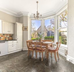 A kitchen with a wooden dining table and chairs near large windows at Fir Trees in Windermere