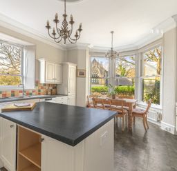 A kitchen with an island countertop dining table and chairs and large windows at Fir Trees in Windermere