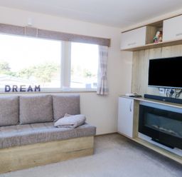 A seating area with a sofa under a large window and a wall-mounted television above an electric fireplace at 31A Foxburrow Hang in Fritton near Belton Norfolk