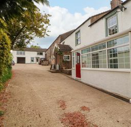A driveway leading to a white house with a red door and a glass conservatory at Kirkland Howe Cottage in Arlecdon