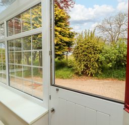 A partially open white door leading to a garden with bushes and trees at Kirkland Howe Cottage in Arlecdon