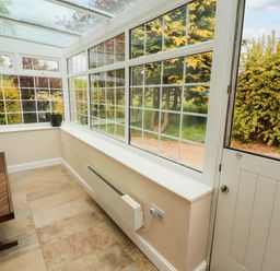 A conservatory with a wooden bench a black plant pot and a heater at Kirkland Howe Cottage in Arlecdon
