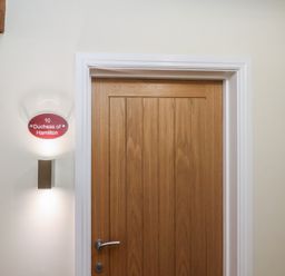 A wooden door with a silver handle and a red sign next to it reading 10 Duchess of Hamilton Whitby