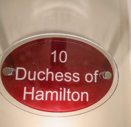 A red oval door plaque with white text reading 10 Duchess of Hamilton