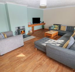 A living room with a gray sectional sofa a wooden coffee table a wood-burning stove and a wall-mounted television at Carreg Yr Onnen in Penparc