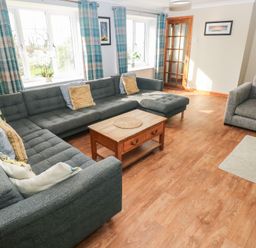 A living room with grey sofas wooden coffee table plaid curtains and framed pictures at Carreg Yr Onnen in Penparc
