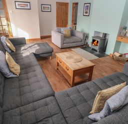 A living room with grey sofas a wood burning stove and a wooden coffee table at Carreg Yr Onnen in Penparc