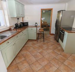A kitchen with green cabinets brown tiled floor and appliances at Carreg Yr Onnen in Penparc