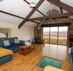 A living room with blue sofas a wood stove large window with a view and wooden ceiling beams at Llwyngwinau Isaf Barn Tynreithyn near Tregaron