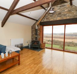 A living room with a wood stove and large windows overlooking fields at Llwyngwinau Isaf Barn in Tynreithyn near Tregaron