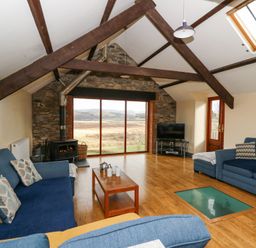 A sitting room with blue sofas a wood stove large window with countryside view and wooden floor at Llwyngwinau Isaf Barn Tynreithyn near Tregaron